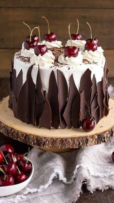 a cake with chocolate and cherries is on a wooden stand next to some cherries