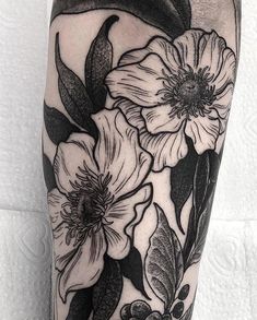 a black and white flower tattoo on the right leg, with leaves and flowers around it