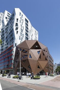 people are walking on the sidewalk in front of some tall buildings with triangular shaped windows