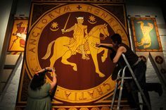 two people are working on a large sign in a room with other paintings behind them