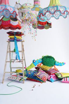 an assortment of colorful lamps and pillows on a white background with a ladder in the foreground