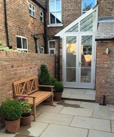 a wooden bench sitting in front of a brick building with potted plants on the side