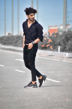 a young man is walking down the street wearing black pants and a blue shirt with his hair pulled back