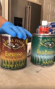 a person in blue gloves and rubber gloves holding two cans of wood stain sitting on top of a counter