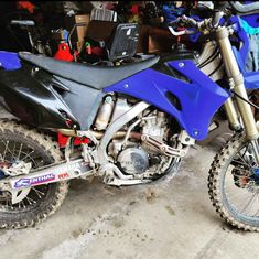 a blue dirt bike parked in front of a pile of other motorbike's