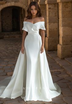 a woman in a white wedding dress standing on a stone walkway with her hands on her hips