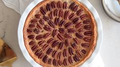 a pecan pie on a white plate next to silverware and utensils