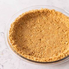 an uncooked pie crust in a glass dish on a marble countertop with a white background