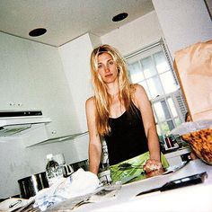 a woman standing in a kitchen next to a counter with food on it and utensils