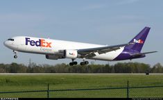 a fedex airplane taking off from an airport runway with trees and grass in the background