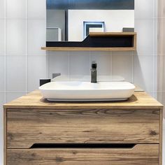 a bathroom sink sitting under a mirror next to a wooden cabinet with drawers underneath it