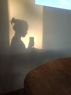 the shadow of a person holding a cell phone in their hand while standing next to a table