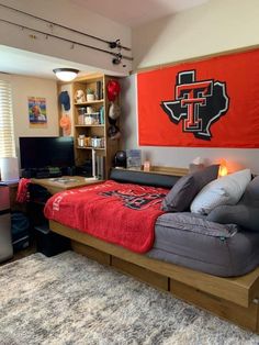 a college dorm room with a bed, desk and computer monitor on the far wall