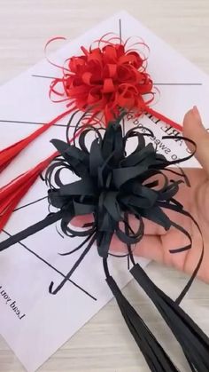 a hand holding some red and black ribbons on top of a piece of white paper