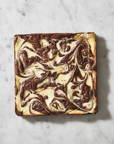 a square brownie with white chocolate swirls on it sitting on a marble surface