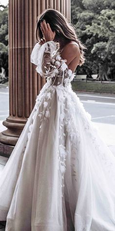 a woman in a white wedding dress standing next to a pillar with her hand on her face