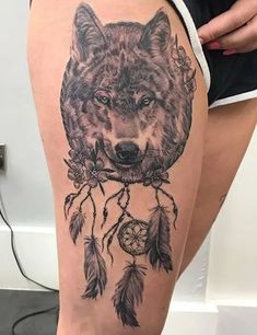 a woman's thigh with a wolf and dream catcher tattoo on the side of her leg