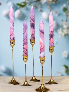 four pink marbled candles are lined up in gold holders on a table with blue background