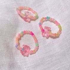 two bracelets with flowers and beads are on a white fabric background, one has a pink teddy bear in the center