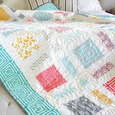 a bed with a colorful quilt on top of it next to a night stand and lamp