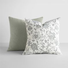 two pillows sitting next to each other on top of a white table with grey and green accents