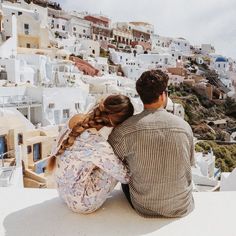 a man and woman sitting on top of a roof looking at the city below them