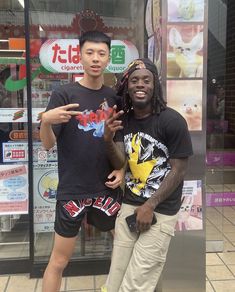 two young men standing next to each other in front of a store window with signs