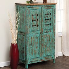 an old green cabinet next to a red vase