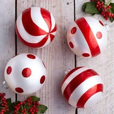 three red and white christmas ornaments sitting on top of a wooden table next to holly