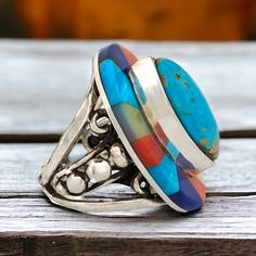 This stunning sterling silver ring, crafted by Robert Drozd featuring a unique multi-stone inlay design, showcasing a harmonious blend of vibrant turquoise, coral, and black onyx stones. Each stone is carefully selected and arranged to evoke the rugged elegance of the canyon landscape, with the turquoise evoking the clear desert skies, the coral recalling the warm hues of sunset, and the black onyx representing the mystery of the canyon's depths. With its expert craftsmanship and Southwestern ch Multicolor Gemstone Accented Ring, Unique Multicolor Large Stone Jewelry, Multicolor Round Gemstones With Stone Setting, Unique Multicolor Jewelry With Large Stone, Multicolor Oval Stone Setting Jewelry, Multicolor Oval Jewelry With Stone Setting, Oval Turquoise Multi-stone Ring In Sterling Silver, Multicolor Sterling Silver Rings With Gemstone Accents, Adjustable Multicolor Stone Rings