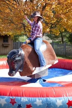 a woman riding on the back of a brown cow in an inflatable obstacle