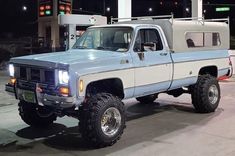 a blue and white pickup truck parked in front of a gas station at night time