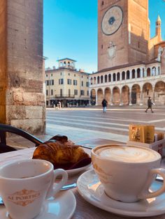 two cups of cappuccino sit on a table in front of a clock tower