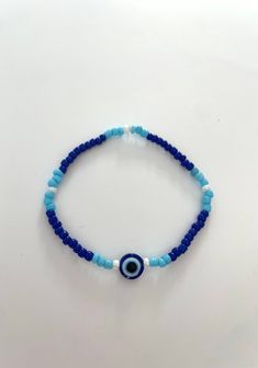 a super cute bracelet with an evil eye in the middle followed by a cute pattern of blues and white! stretchy and durable. Blue Spiritual Stretch Bracelet For Beach, Spiritual Blue Stretch Bracelet For Beach, Evil Eye Bead Bracelet, Adjustable Blue Evil Eye Bracelet Hand-strung, Adjustable Blue Hand-strung Evil Eye Bracelet, Bohemian Friendship Bracelets With Evil Eye, Spiritual Blue Stretch Bracelet With Letter Beads, Adjustable Turquoise Beaded Bracelets With Evil Eye, Blue Evil Eye Bracelet With Round Beads