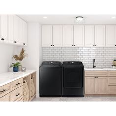 a black washer and dryer sitting in a kitchen next to white cupboards