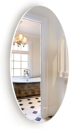 an oval mirror reflecting a bathtub in a bathroom with black and white tile flooring