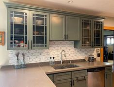 a kitchen with green cabinets and white tile backsplash, stainless steel sink and dishwasher