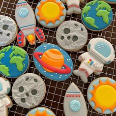 decorated cookies with space related items on a cooling rack, including an astronaut's spaceship and rocket ship