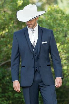 a man in a blue suit and white cowboy hat is looking down at his hand