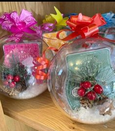 two snow globes with christmas decorations in them sitting on a wooden shelf next to ribbons and bows