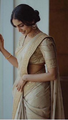 a woman in a white sari and gold jewelry is looking down at her hand