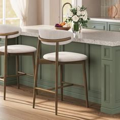 two white stools sitting in front of a kitchen island with marble counter tops and green cabinets