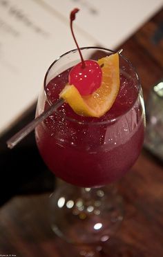 a red drink with a cherry garnish on the rim and a slice of orange