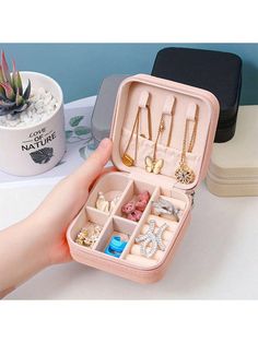 an open pink jewelry box sitting on top of a white table next to a potted plant