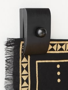 a close up of a black and gold rug with a metal hook on the wall