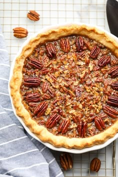 a pie with pecans in it on a cooling rack next to a blue towel