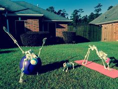 two skeletons are on yoga mats in the yard, one is upside down and another is standing up