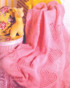 a knitted pink blanket next to a yellow teddy bear