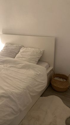 a bed with white sheets and pillows in a room next to a basket on the floor