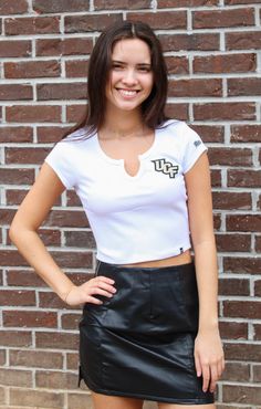 Shopping for cute game day gear? We've got you covered! The UCF Cropped Cali Tee is the perfect addition to your closet. This top features a scoop v-neckline and ribbed material for a comfortable and flattering fit. The school logo on the front gives this tee a sleek and spirited look. Whether heading to class or a tailgate, this top is a must-have! Pair with a cute skirt or shorts for the perfect look! Details: *OFFICIALLY LICENSED* True to size Stretchy Ribbed Material Scoop V-Neckline 95% cot Sporty V-neck Top For College, Stretch V-neck Top For Streetwear, Casual V-neck Top For College, Varsity Fitted Top For Game Day, Collegiate Style Cotton V-neck Top, V-neck Spring College Tops, White Stretch School Spirit Top, White Stretch Tops For School Spirit, College Style Tops For Game Day In Spring